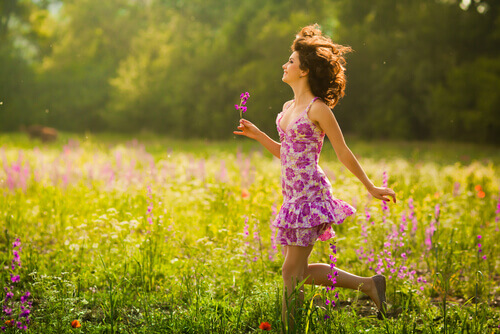 Mulher caminhando entre as flores sorridente e feliz