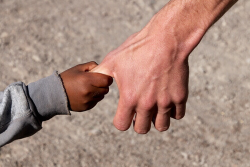 Mão de um menino negro segurando a de um homem branco