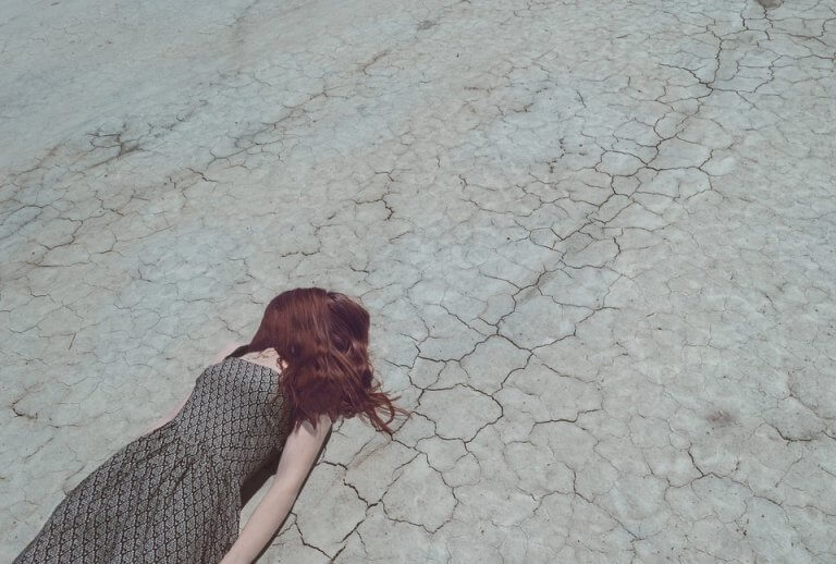Mulher deitada em chão árido e seco