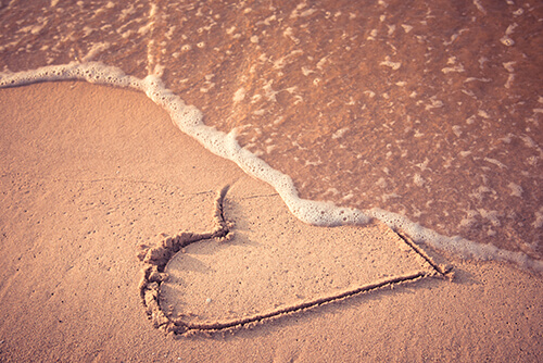 Onda apagando coração desenhado na areia