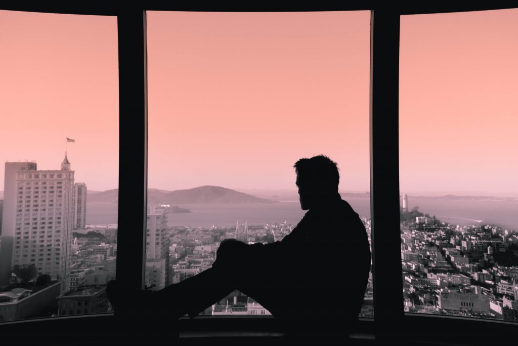 Homem olhando pela janela ao entardecer