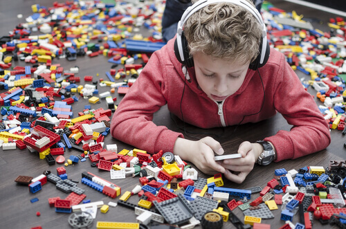 Menino brincando no celular com legos em volta