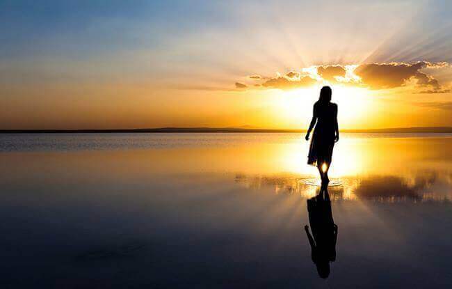 Mulher em praia diante do por do sol