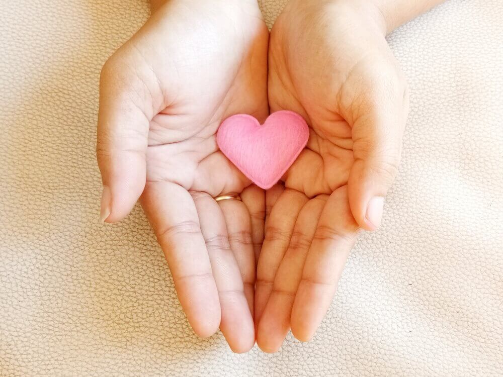 Mãos segurando coração cor-de-rosa