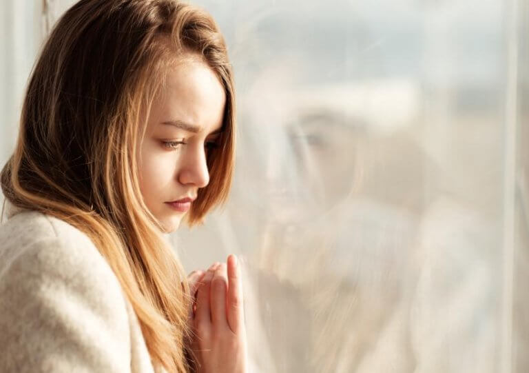 Mulher pensativa diante de janela