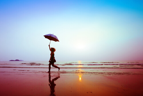 Mulher caminhando em praia com guarda-chuva