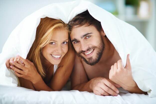 Casal sorrindo sob os lençóis