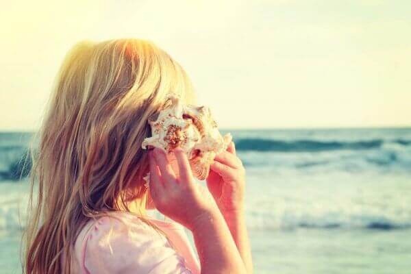 Menina ouvindo concha na praia