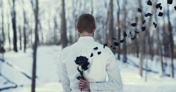 Homem escondendo flor preta com as pétalas voando