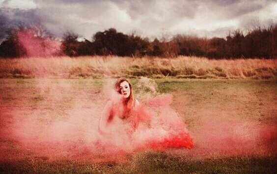 Mulher sentada na grama com fumaça colorida