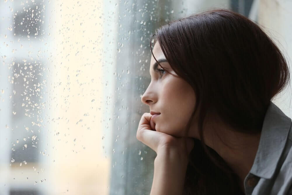 Mulher observando chuva na janela
