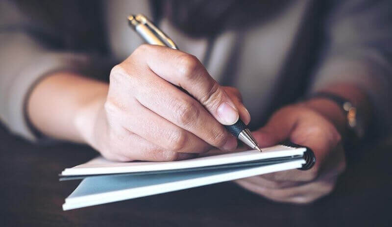 Pessoa escrevendo em caderno