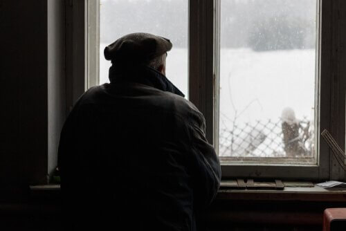 Homem observando neve pela janela