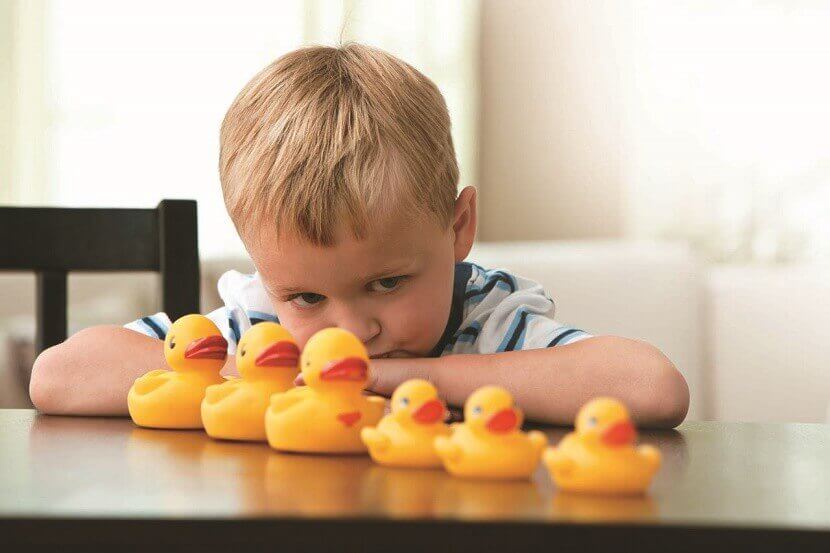 Menino com autismo olhando patos de borracha