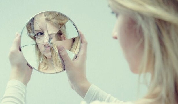 Mulher se olhando em espelho quebrado