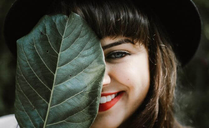 Mulher sorrindo atrás de folha
