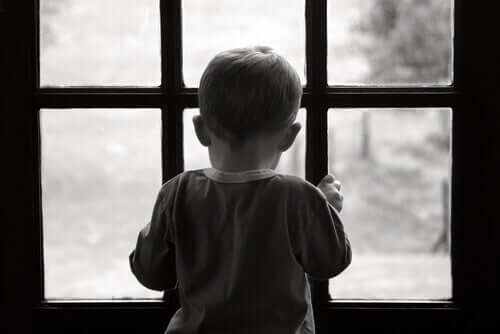 Criança triste diante de janela