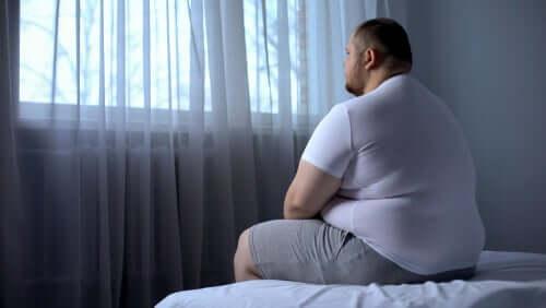 Homem obeso sentado em sua cama
