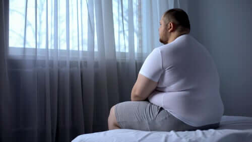 Homem obeso sentado em sua cama