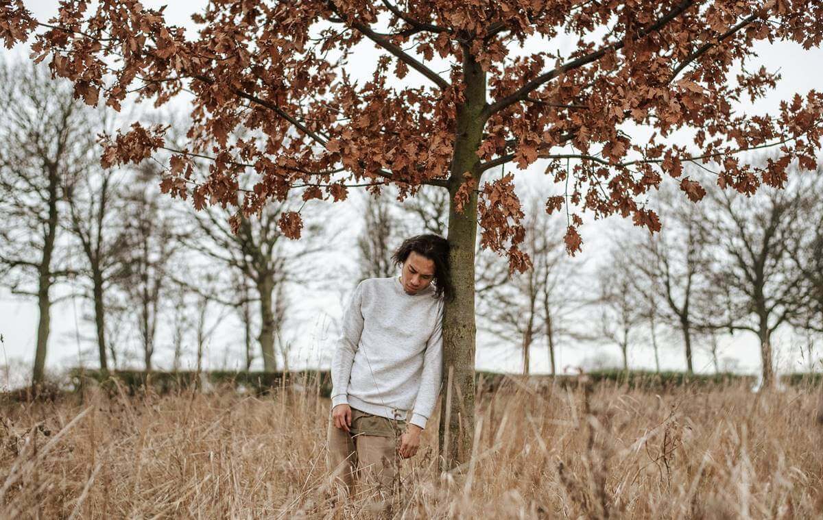 Jovem apoiado em árvore